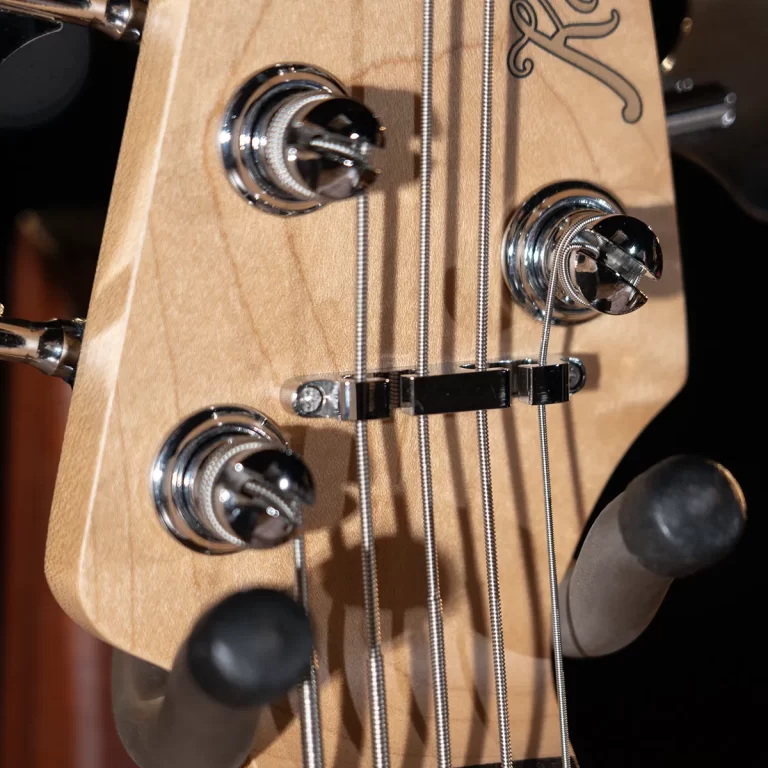 Close-up of a wooden guitar headstock with chrome tuning pegs, six steel strings, and a decorative logo. ขายราคาพิเศษ