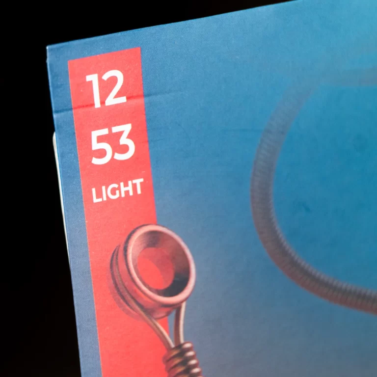 Close-up of a blue product box with a red vertical label showing '12 53' and 'LIGHT', with a metallic component at the bottom left on a dark background. ขายราคาพิเศษ