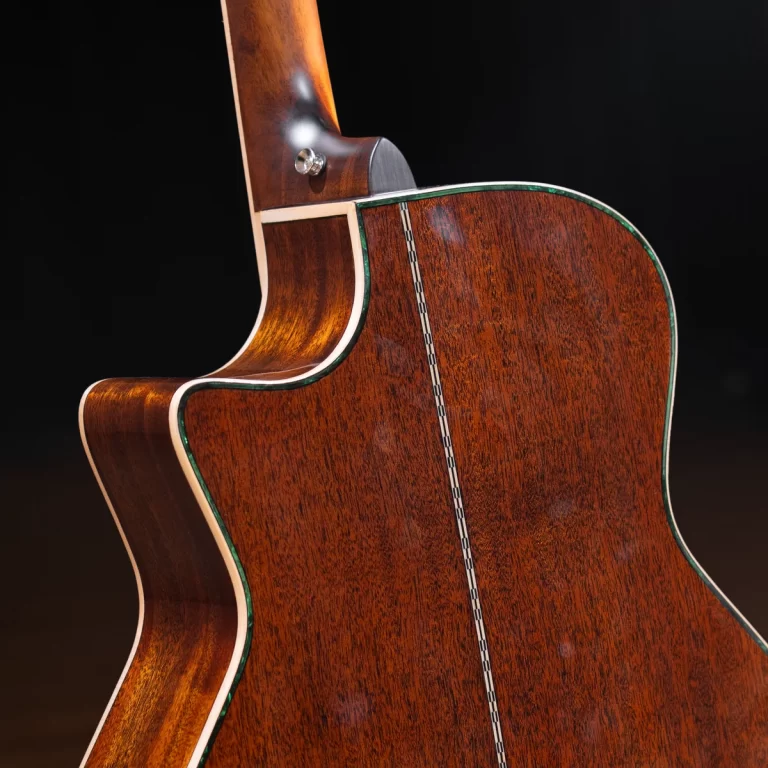 Close-up of the back and side of a polished wooden acoustic guitar with green binding and decorative inlay, showing its curved shape and glossy finish ขายราคาพิเศษ