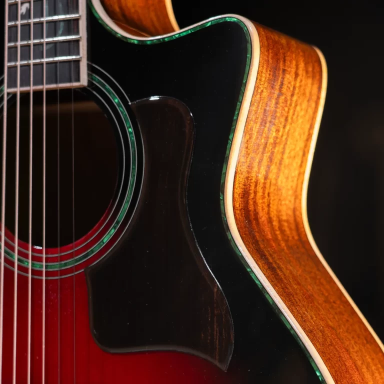 Close-up of an acoustic guitar: glossy black top with green binding, a red interior around the soundhole, and a warm wood side. ขายราคาพิเศษ