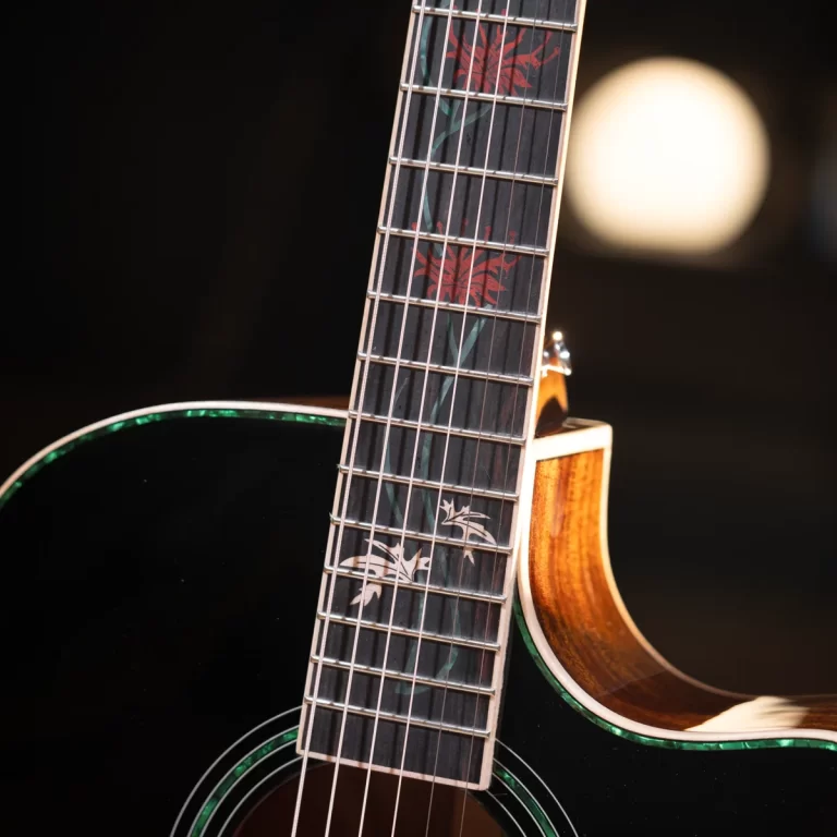 Close-up of a guitar neck with a dark fretboard featuring red leaf inlays and a glossy black body with green binding. ขายราคาพิเศษ