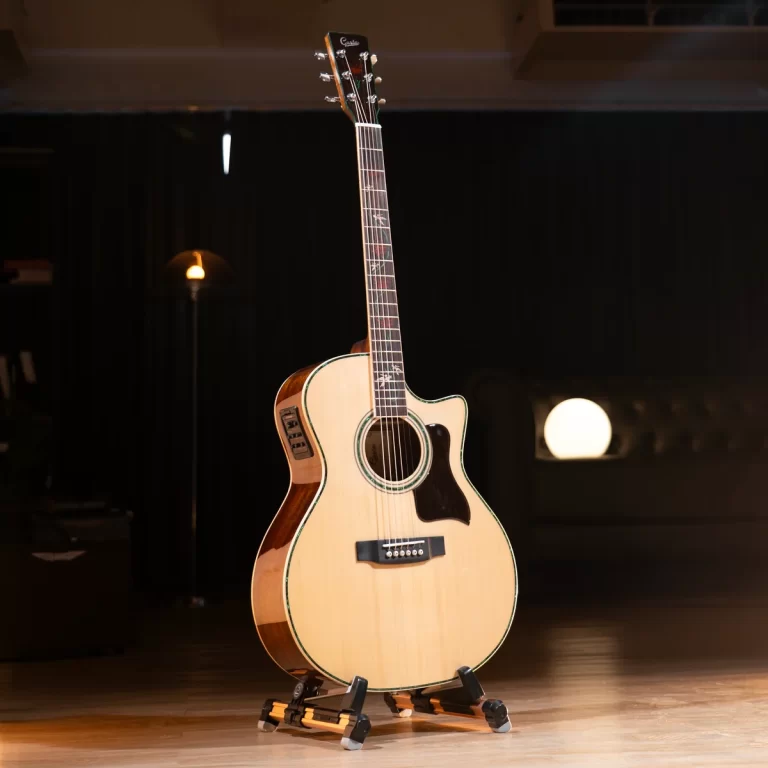 Cream-colored acoustic guitar on a stand in a dimly lit stage with a warm spotlight on the body. ขายราคาพิเศษ