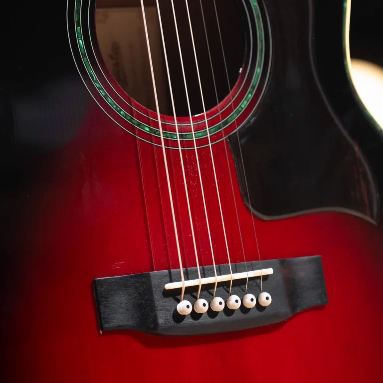 Close-up of a red sunburst acoustic guitar showing the soundhole, six strings over the bridge with white bridge pins and saddle detail. ขายราคาพิเศษ