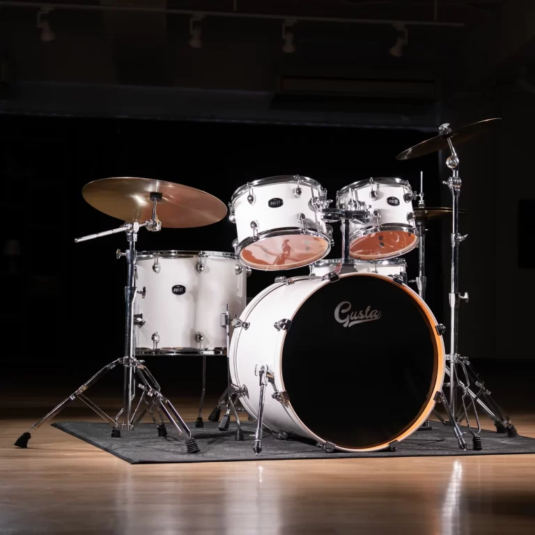 White drum kit on a dark stage with a black bass drum displaying the Gusta logo, chrome hardware gleaming. ขายราคาพิเศษ