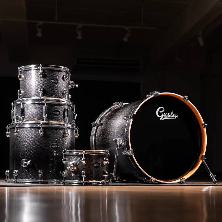 Sparkly black drum set on a dark stage, with a large bass drum labeled 'Gusta' and stacked toms and snare nearby in a studio setting. ขายราคาพิเศษ