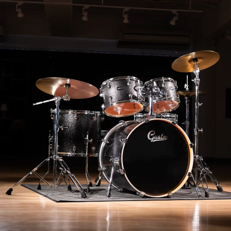 Full drum kit on a wooden stage with cymbals and a black bass drum labeled 'Gusta' under warm stage lighting. ขายราคาพิเศษ