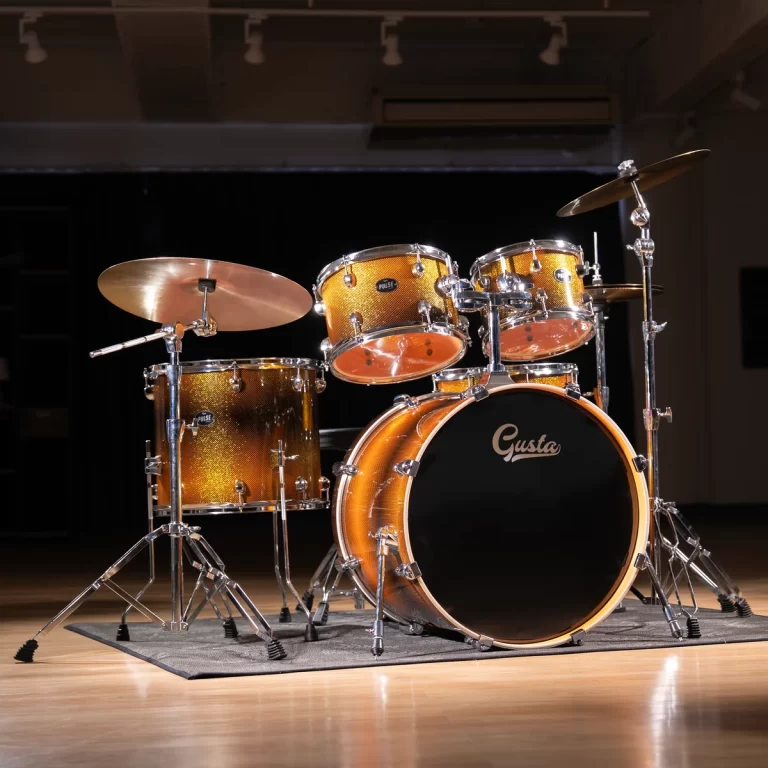 Golden drum kit with a black bass drum labeled 'Gusta' on a stage, chrome hardware, and a cymbal setup ready to play on a wooden floor. ขายราคาพิเศษ