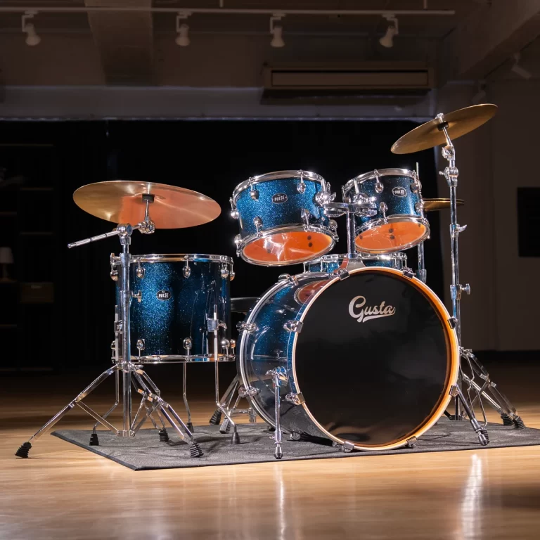 Blue glitter drum kit on a wooden stage with cymbals and a bass drum labeled 'Gusta' ready for performance. ขายราคาพิเศษ