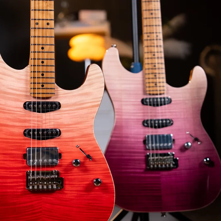 Two electric guitars with sunburst orange-to-red and pink-to-purple finishes, hanging side by side in a dim showroom. ขายราคาพิเศษ
