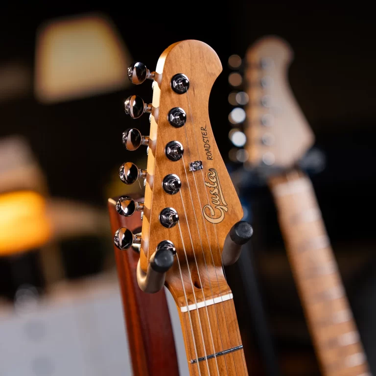 Close-up of a wooden guitar headstock with chrome tuning pegs; brand logo visible in focus, background blurred. ขายราคาพิเศษ
