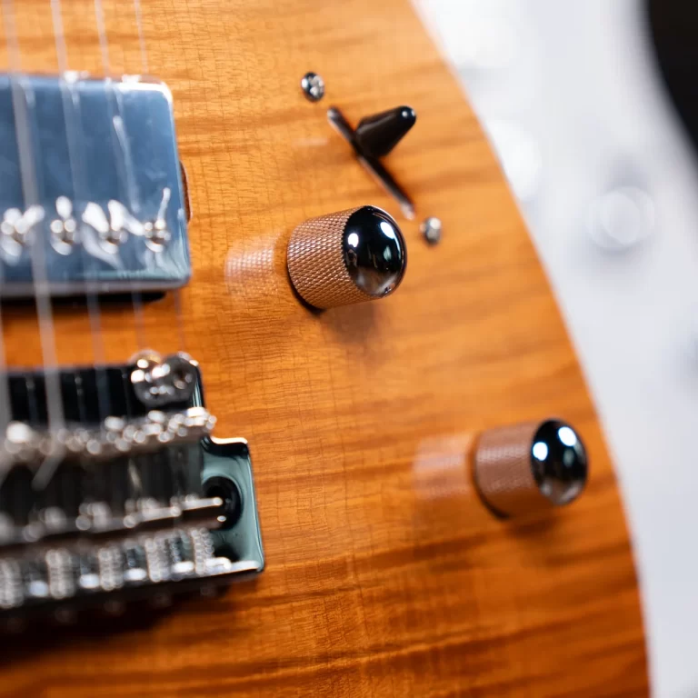 Close-up of an electric guitar body with amber wood grain, showing knurled metal knobs and a pickup ขายราคาพิเศษ