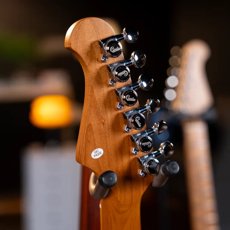 Close-up of a wooden guitar headstock with six chrome tuning pegs and a small QC PASS sticker visible on the wood. ขายราคาพิเศษ
