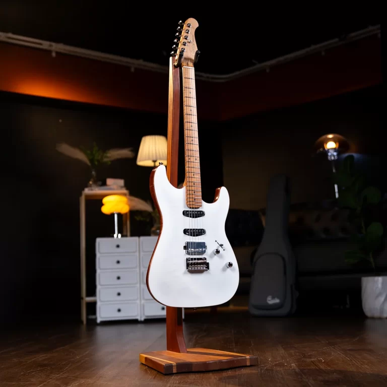 White electric guitar on a wooden stand in a dim studio, with a guitar case and cabinet in the background ขายราคาพิเศษ