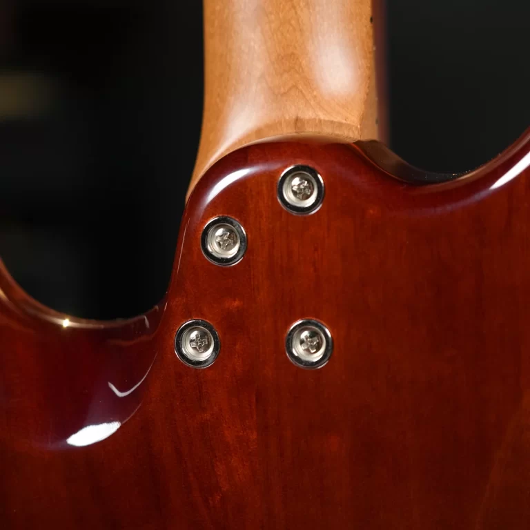 Close-up of a glossy brown electric guitar body where the neck meets the body, showing chrome screws and wooden finish ขายราคาพิเศษ