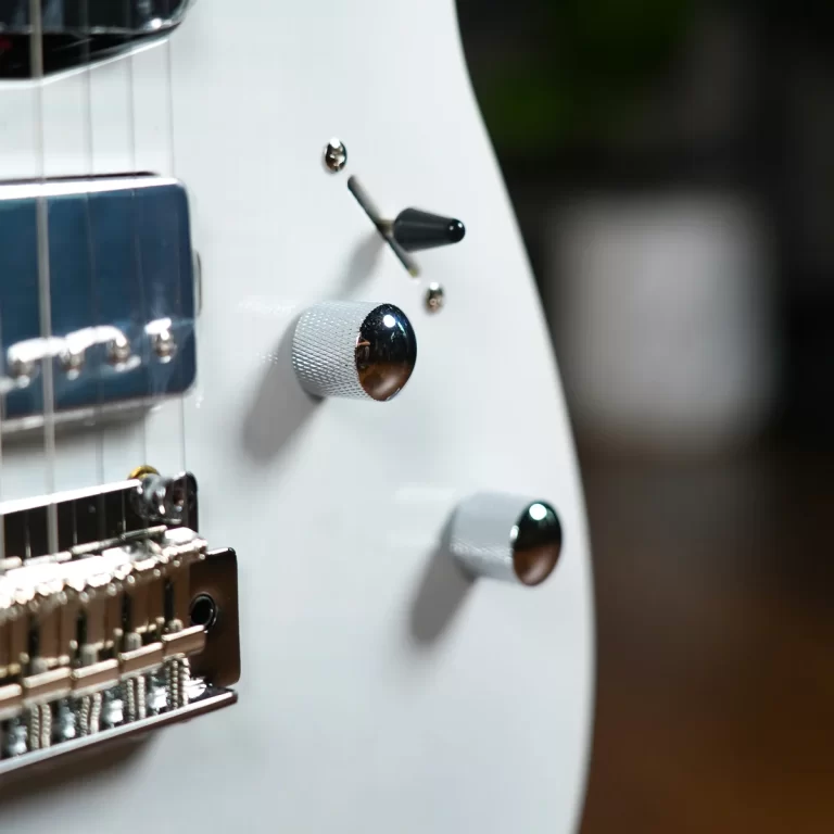 Close-up of a white electric guitar showing knobs, a toggle switch, and part of the bridge surface. ขายราคาพิเศษ