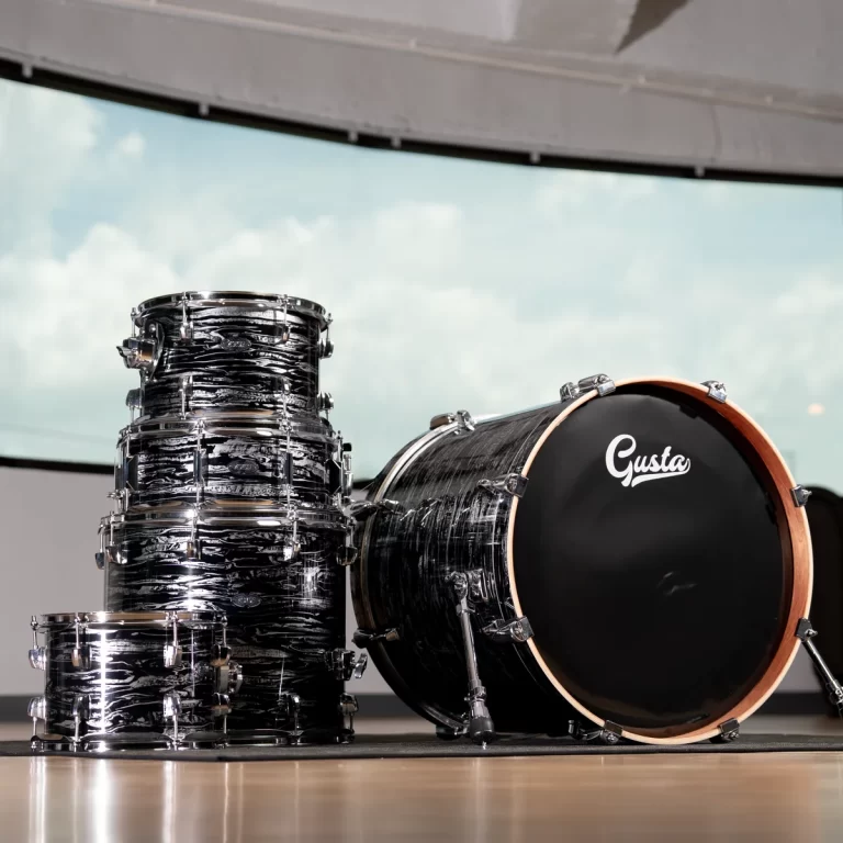 Black marbled drum set with chrome hardware, including a stacked toms and a large bass drum with a wooden rim and 'Gusta' logo in a studio. ขายราคาพิเศษ