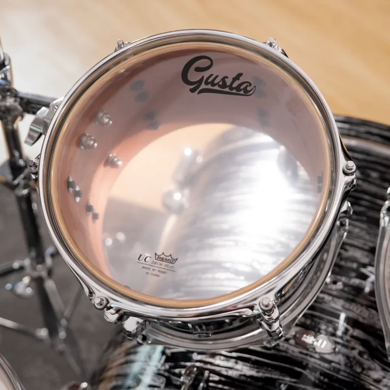 Close-up of a drum head showing the 'Gusta' logo, with chrome hardware and the inner shell visible through the head. ขายราคาพิเศษ
