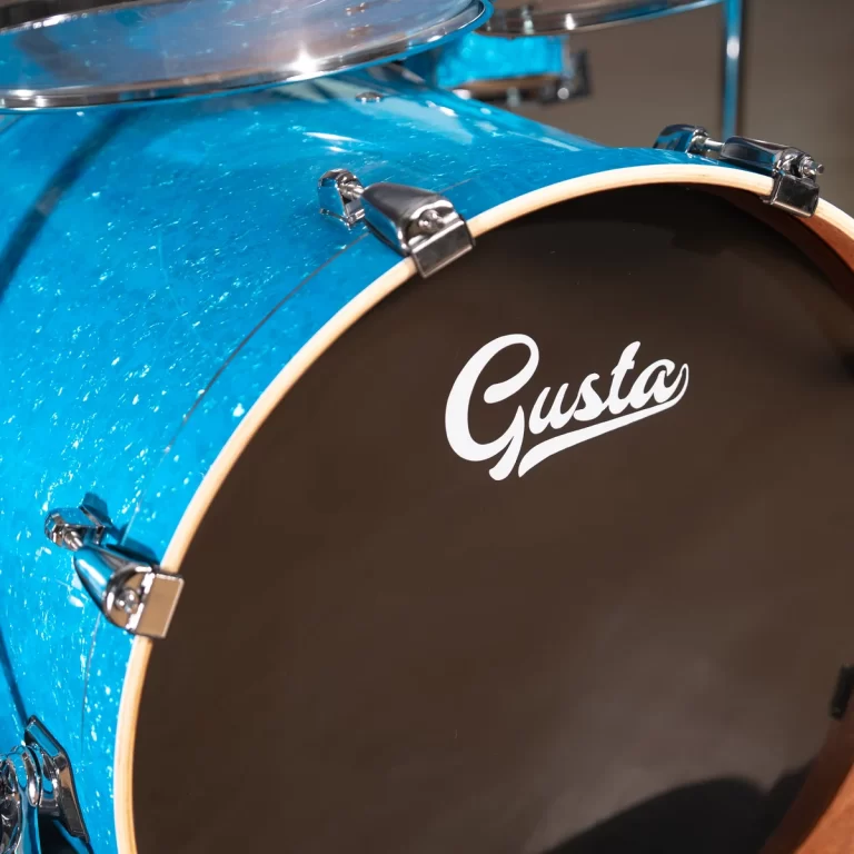 Close-up of a blue drum shell with chrome hardware and a black bass drum head reading 'Gusta'. ขายราคาพิเศษ