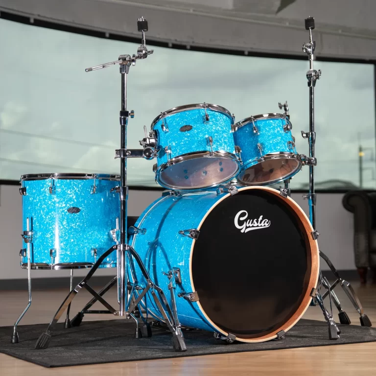 Blue sparkle drum kit on a black stage carpet, featuring a bass drum with the 'Gusta' logo and two mounted toms above it. ขายราคาพิเศษ