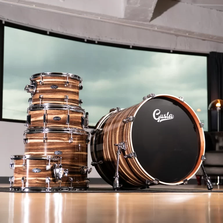 Wooden drum set with stacked toms and a large bass drum labeled 'Gusta' in a bright studio. ขายราคาพิเศษ