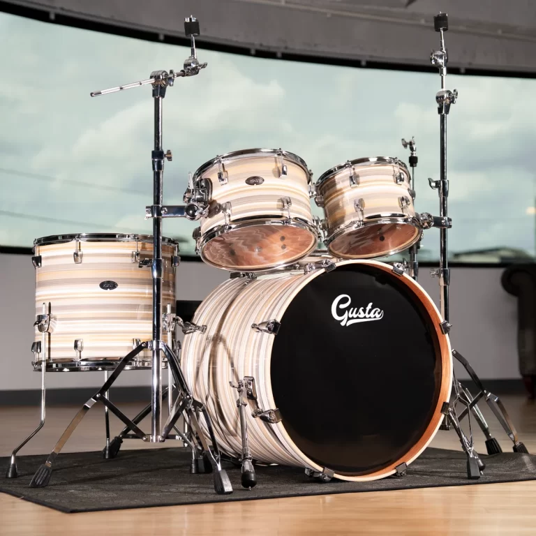 Drum kit with striped shells on a stage, bass drum bearing the Gusta logo in the foreground. ขายราคาพิเศษ