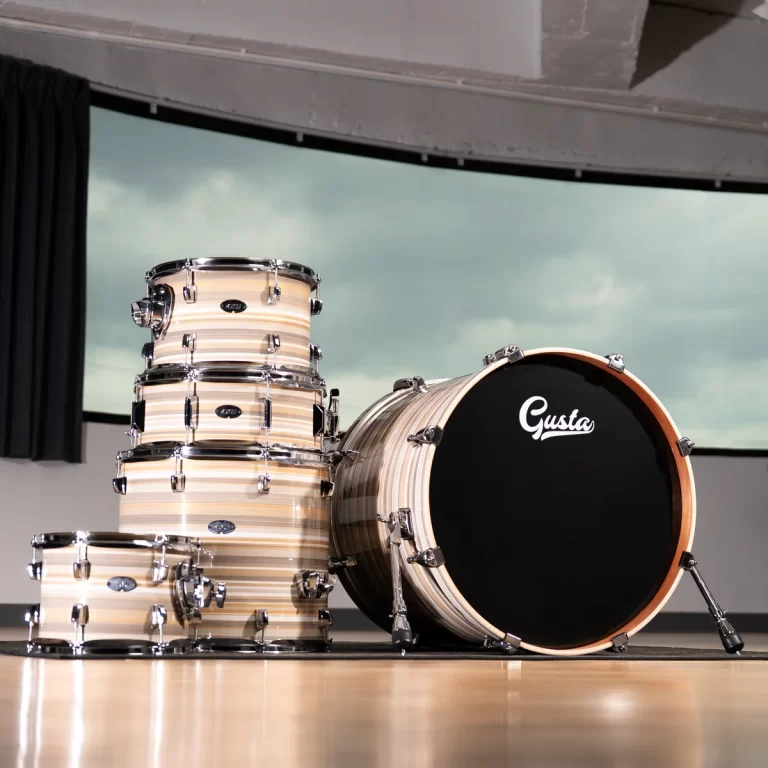 Beige striped drum kit stacked on a wooden floor in a studio, bass drum with 'Gusta' logo on the front ขายราคาพิเศษ