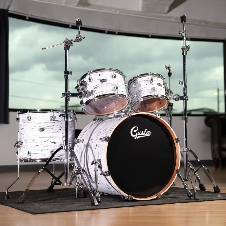 White marbled drum kit with a black bass drum head labeled 'Gusta' on a wooden stage rug. ขายราคาพิเศษ