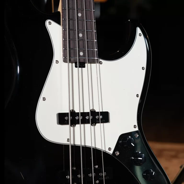 Close-up of a black electric bass guitar with a white pickguard, showing strings, pickup, and control knobs on stage lighting. ขายราคาพิเศษ