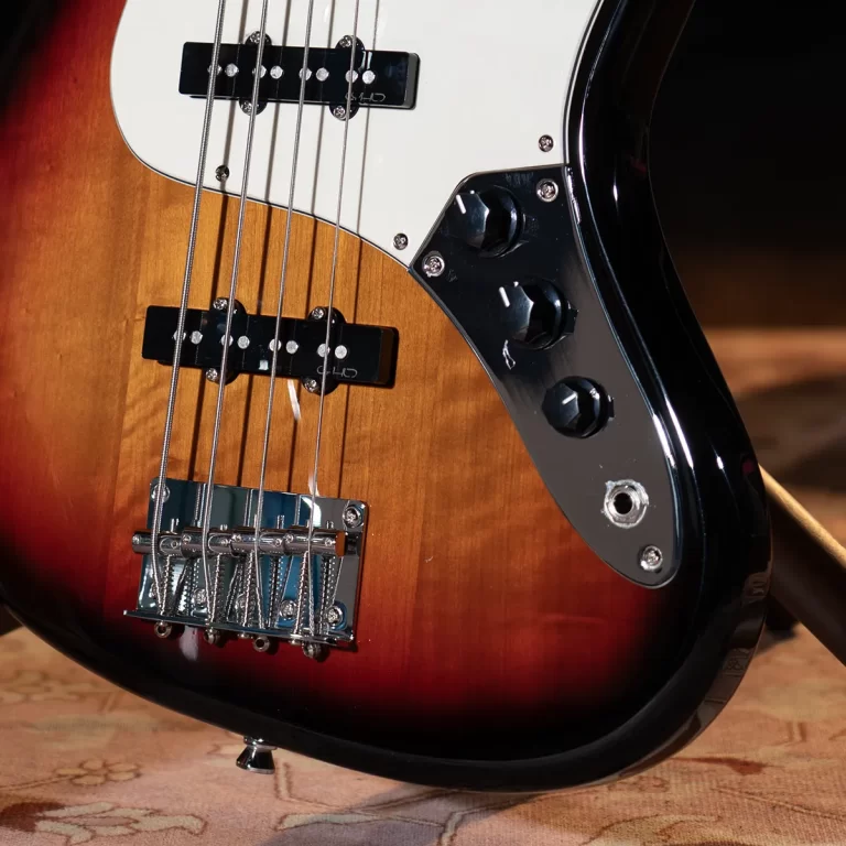 Close-up of a sunburst electric bass guitar body showing two pickups, strings, bridge, and chrome control plate with knobs on the right edge. ขายราคาพิเศษ