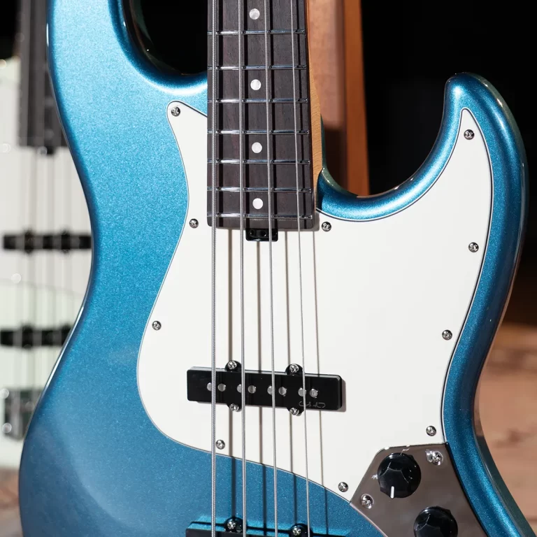 Close-up of a metallic blue electric bass guitar with a white pickguard and silver strings. ขายราคาพิเศษ