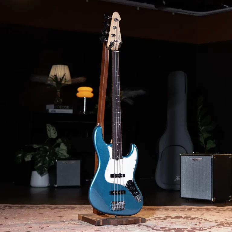 Blue electric bass guitar on a stand in a dim studio, with a small amplifier and guitar case visible in the background. ขายราคาพิเศษ