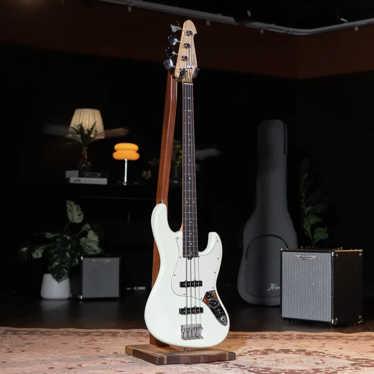 Mint green electric bass guitar on a wooden stand in a dim room, with an amp and guitar case in the background. ขายราคาพิเศษ