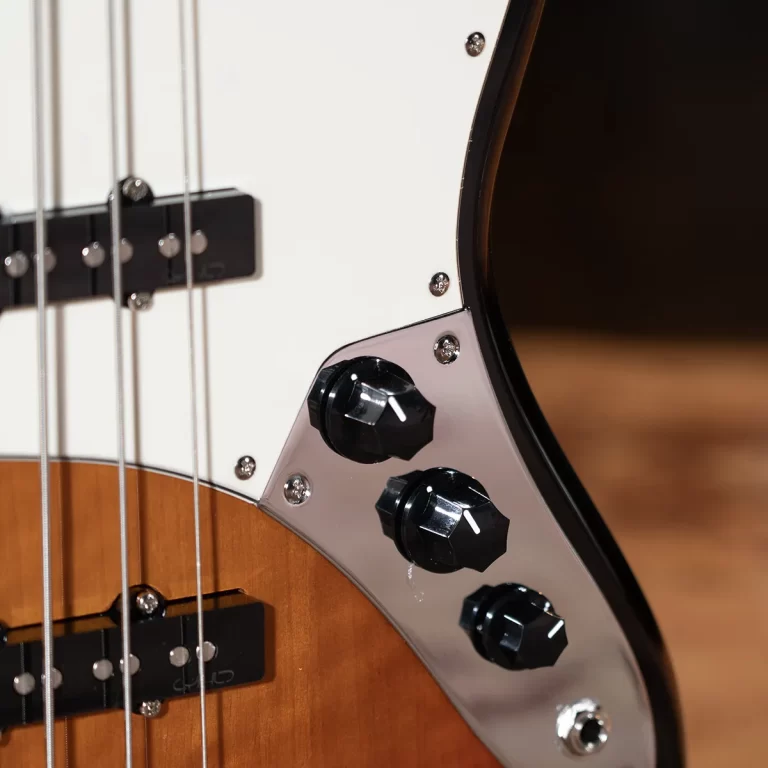Close-up of a bass guitar showing strings, pickups, and three black control knobs on a chrome pickguard. ขายราคาพิเศษ