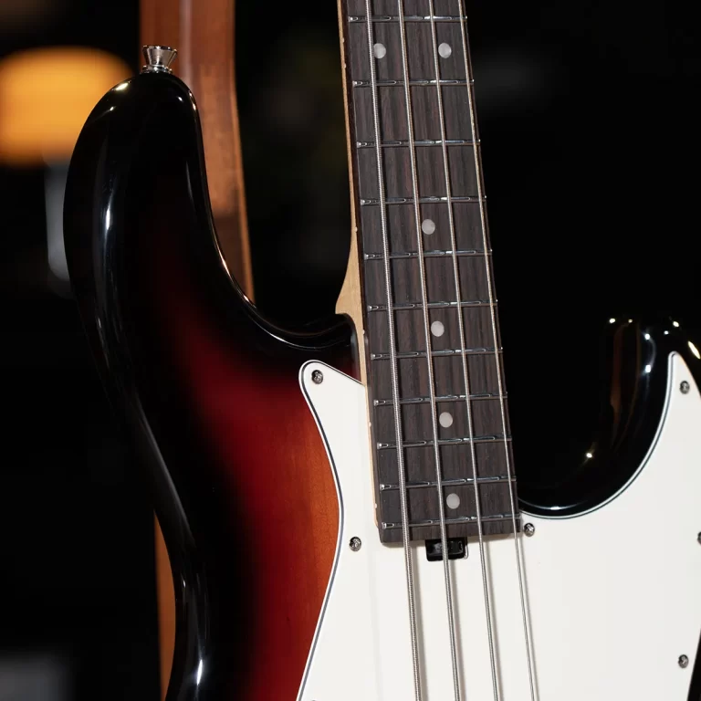 Close-up of a sunburst electric bass guitar neck and body with a white pickguard and metal strings. ขายราคาพิเศษ