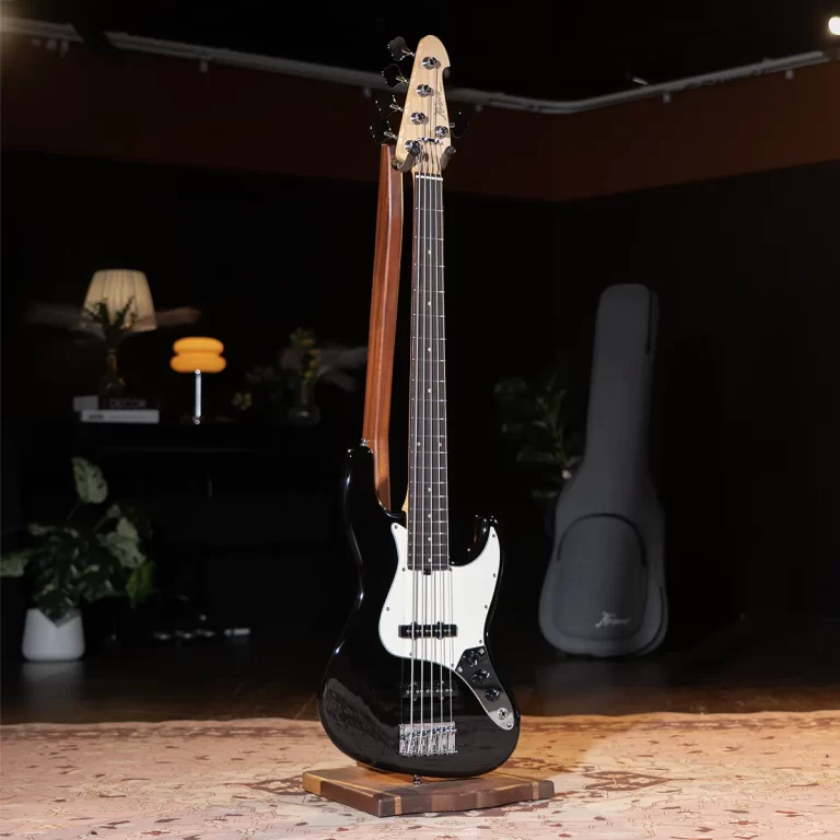 Black electric bass guitar on a wooden stand in a dim studio, with a guitar case in the background. ขายราคาพิเศษ
