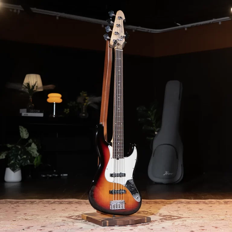 Sunburst electric bass guitar on a wooden stand in a dim studio with a guitar case in the background ขายราคาพิเศษ
