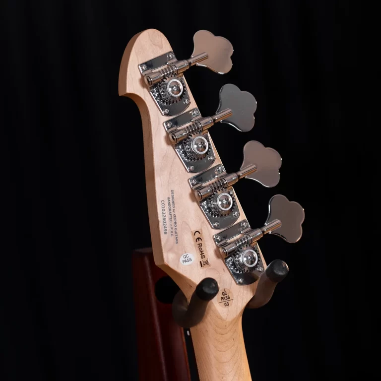 Close-up of a wooden bass guitar headstock with chrome tuning pegs against a black background ขายราคาพิเศษ