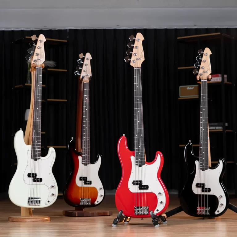Four electric bass guitars on stands lined up in a music shop, white, sunburst, red, and black models against a black curtain backdrop on a wooden floor, showcasing diverse finishes. ขายราคาพิเศษ