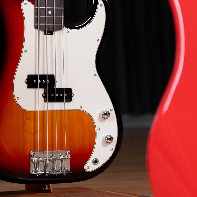 Close-up of a sunburst bass guitar body with a white pickguard, pickups, and strings showing on a wooden floor. ขายราคาพิเศษ