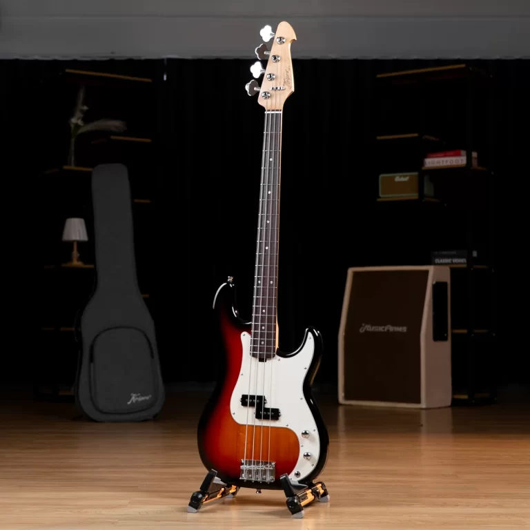 Sunburst electric bass guitar on a stand in a dim studio with amplifiers and a guitar case in the background ขายราคาพิเศษ