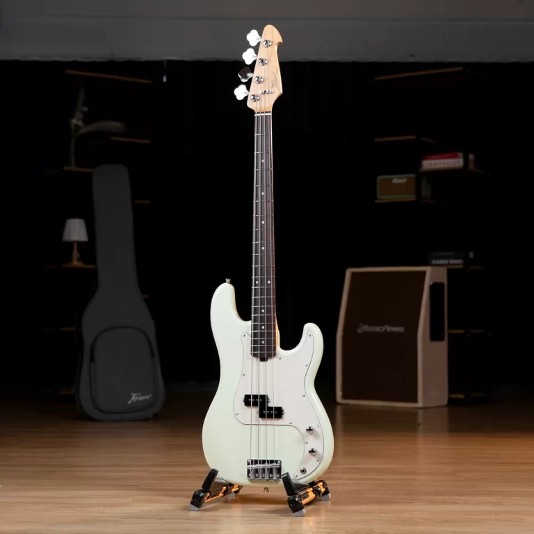 White electric bass guitar on a stand, in a dimly lit practice room with amplifiers in the background. ขายราคาพิเศษ