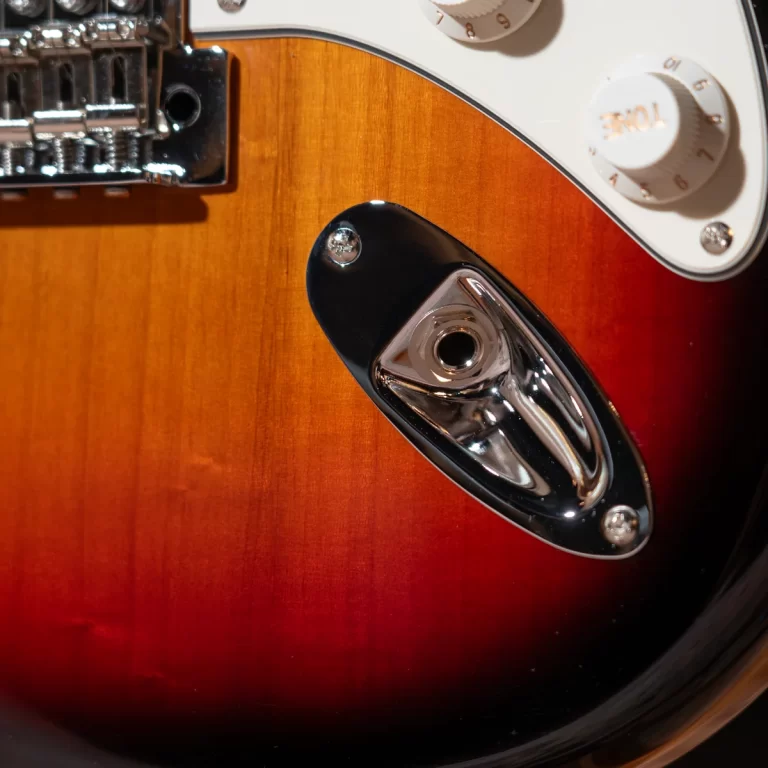 Close-up of a sunburst electric guitar body, showing the tremolo bridge on the left and a chrome plate with a recessed output jack on the right. ขายราคาพิเศษ