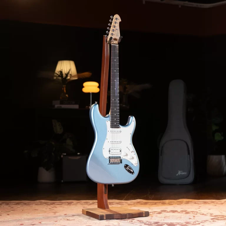 Blue electric guitar on a wooden stand in a dim room, with a guitar case in the background. ขายราคาพิเศษ