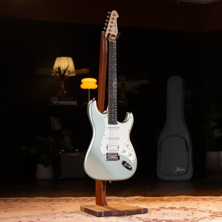 Fender Stratocaster-style electric guitar in pale blue on a wooden stand in a dim studio with warm lamps in the background, white pickguard visible. ขายราคาพิเศษ