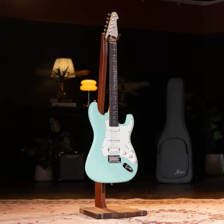 Turquoise Fender-style electric guitar on a wooden stand in a dim room with warm lighting and a guitar case in the background ขายราคาพิเศษ