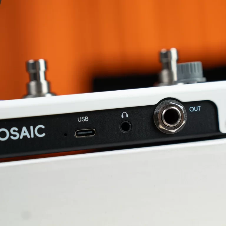 Close-up of a white audio device's rear panel showing a USB port, a 3.5mm headphone jack, and a 1/4-inch output jack against an orange background with part of the MOSAIC label visible. ขายราคาพิเศษ
