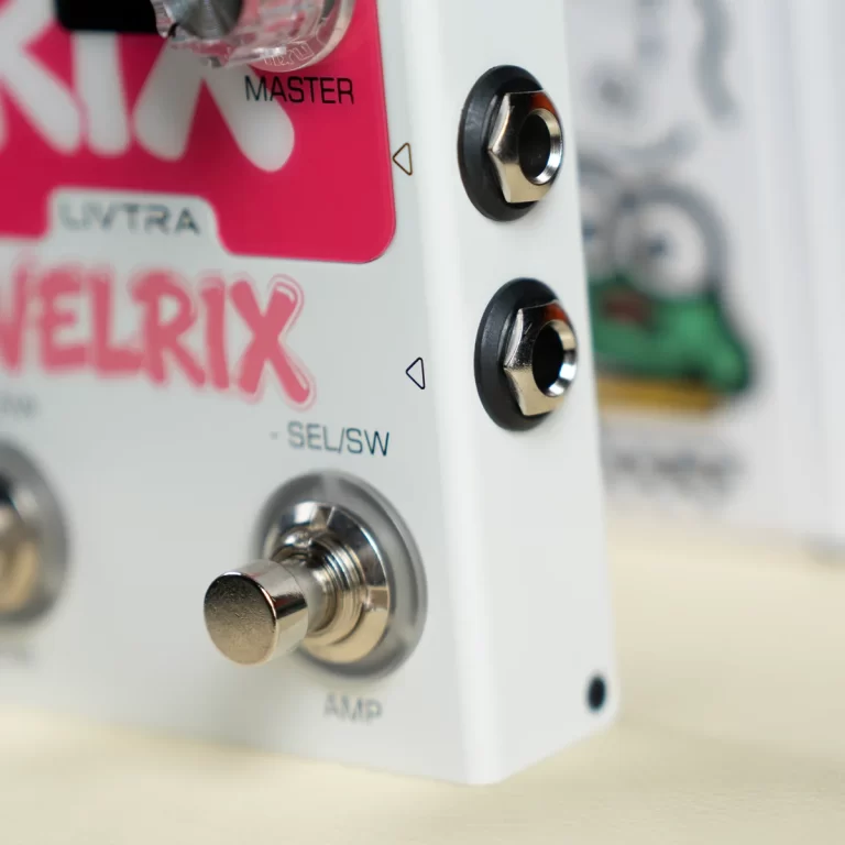 Close-up of a white electronic device panel with a pink VelRIX label, showing a metal push button and two 1/4-inch jacks. ขายราคาพิเศษ