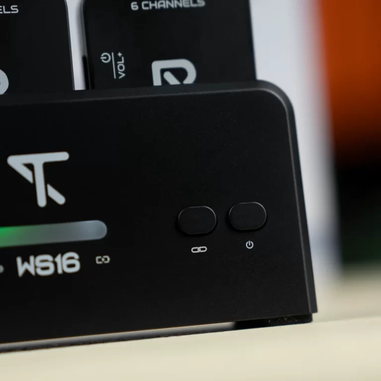 Close-up of a black charging dock with two rounded buttons and a power icon; a white chain-link symbol suggesting pairing or connectivity, with a blurred device in the background. ขายราคาพิเศษ
