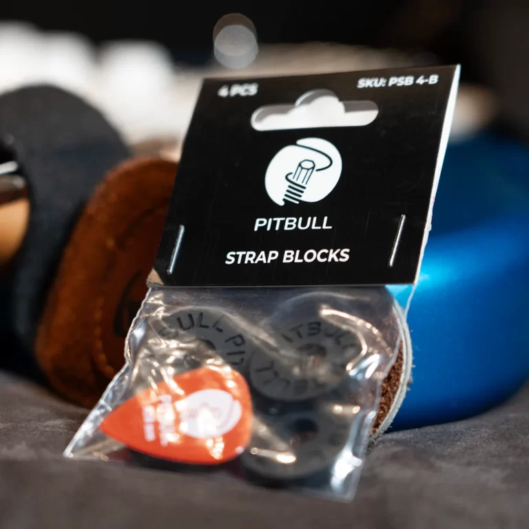 Pitbull Strap Blocks packaging: black tag with logo and '4 PCS', SKU PSB 4-B, and a plastic bag with hardware and an orange guitar pick beneath. ขายราคาพิเศษ