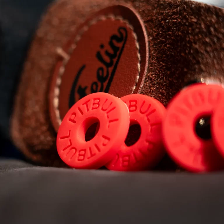 Close-up of red donut-shaped beads with holes, stacked near a brown suede surface with a stitched leather patch in the background. ขายราคาพิเศษ